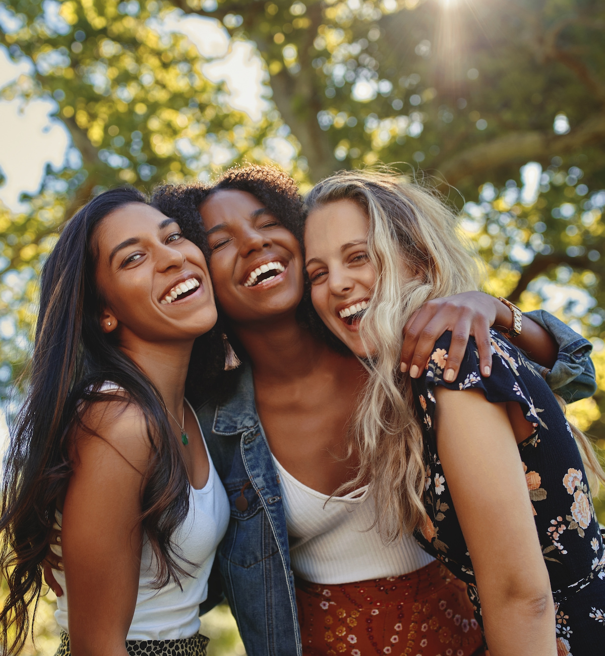 Cheerful excited positive modern group of female friends hugging together in park and laughing and having fun